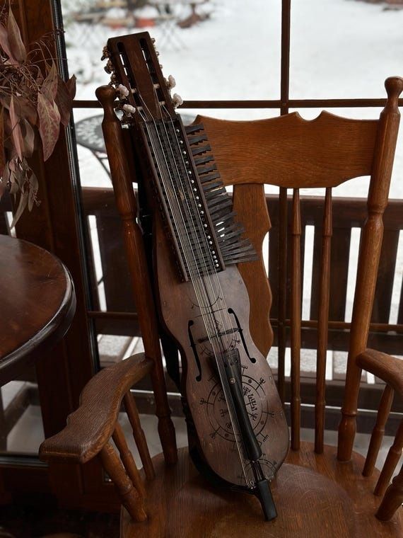 En tränyckelharpa lutar mot en trästol framför ett snötäckt fönster